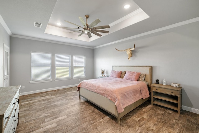 bedroom with wood-type flooring, a raised ceiling, ceiling fan, and ornamental molding