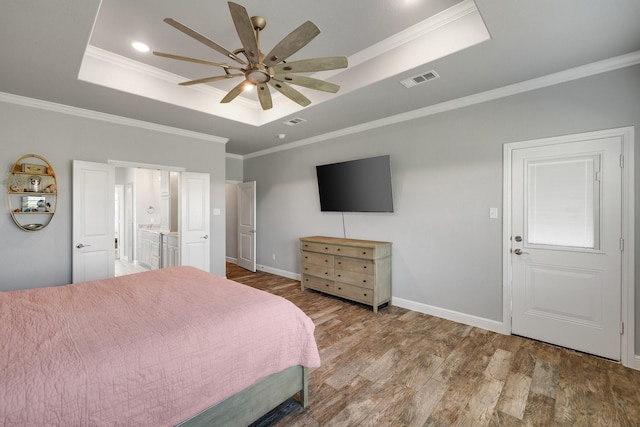 bedroom with ensuite bath, hardwood / wood-style floors, ceiling fan, a tray ceiling, and ornamental molding