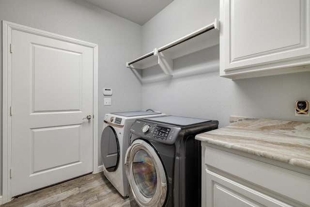 clothes washing area featuring cabinets, washing machine and clothes dryer, and light hardwood / wood-style floors