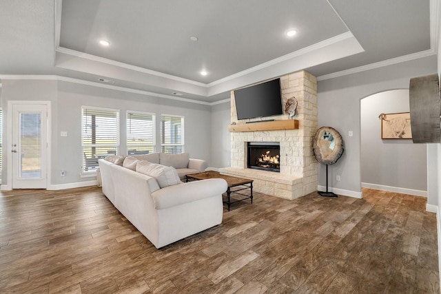 living room featuring a tray ceiling, a fireplace, ornamental molding, and hardwood / wood-style flooring