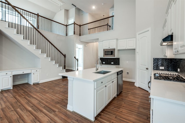 kitchen with white cabinets, a towering ceiling, stainless steel appliances, an island with sink, and sink