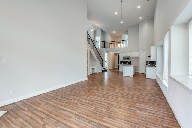 unfurnished living room with light hardwood / wood-style floors, sink, a notable chandelier, and a towering ceiling