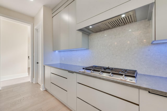 kitchen with wall chimney range hood, stainless steel gas stovetop, light hardwood / wood-style flooring, and tasteful backsplash