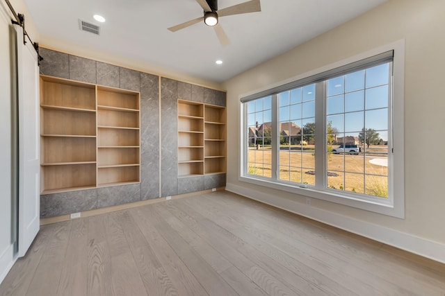 interior space featuring ceiling fan, a barn door, light hardwood / wood-style floors, and multiple windows