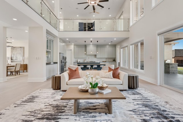 living area featuring light wood finished floors, baseboards, a high ceiling, and ceiling fan