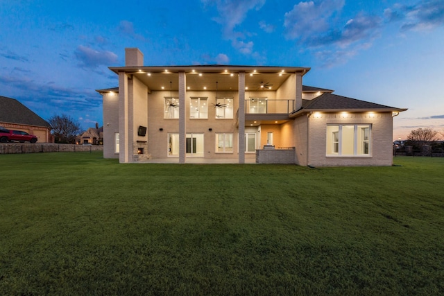 back house at dusk featuring a yard, a balcony, and a patio