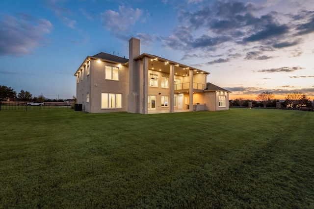 back house at dusk featuring a balcony, central AC, and a lawn