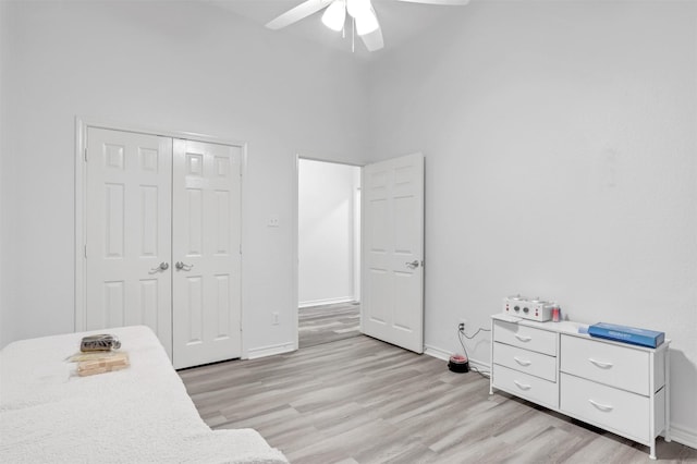 bedroom featuring a high ceiling, light wood-type flooring, ceiling fan, and a closet