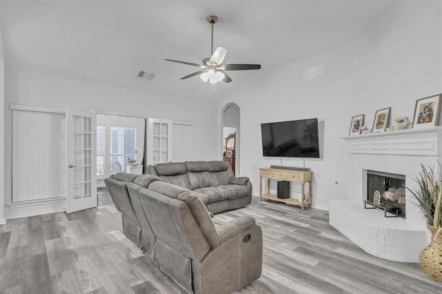 living room featuring a fireplace, vaulted ceiling, french doors, ceiling fan, and light hardwood / wood-style flooring