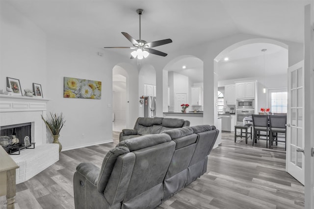 living room with lofted ceiling, a brick fireplace, ceiling fan, and light wood-type flooring