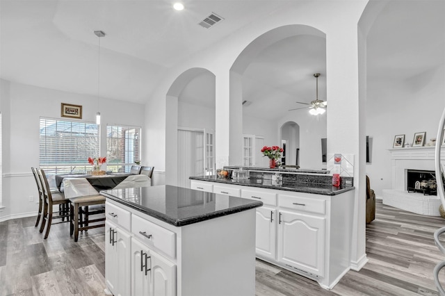 kitchen featuring decorative light fixtures, white cabinets, ceiling fan, dark stone counters, and a kitchen island