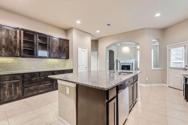 kitchen featuring stainless steel dishwasher, an island with sink, light tile patterned floors, dark brown cabinets, and sink