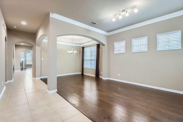 empty room with a notable chandelier, light wood-type flooring, and crown molding