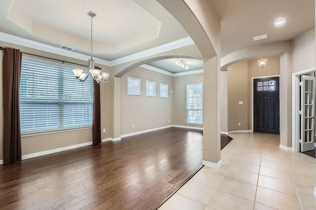 entrance foyer with light wood-type flooring, a notable chandelier, a tray ceiling, and crown molding