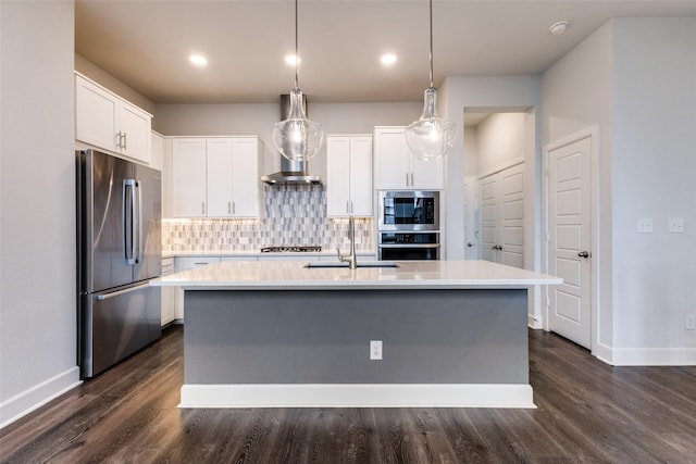 kitchen with appliances with stainless steel finishes, white cabinets, decorative light fixtures, and a center island with sink