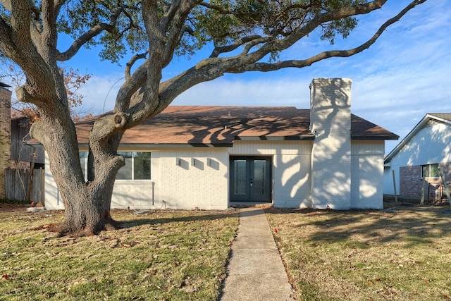 view of front facade featuring roof with shingles, a chimney, a front lawn, and french doors