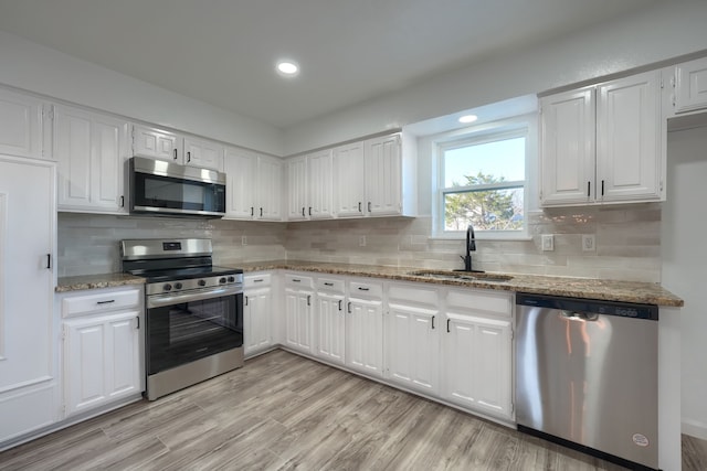 kitchen with stainless steel appliances, white cabinets, a sink, and light wood finished floors