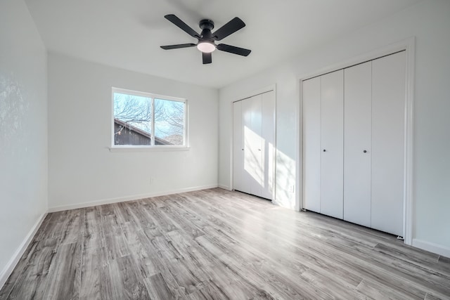 unfurnished bedroom featuring wood finished floors, ceiling fan, baseboards, and two closets