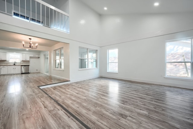 unfurnished living room with high vaulted ceiling, light wood-type flooring, baseboards, and an inviting chandelier