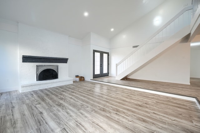 unfurnished living room featuring a brick fireplace, stairway, wood finished floors, and french doors