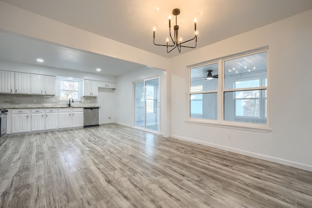 interior space with light wood finished floors, backsplash, stainless steel dishwasher, a sink, and a chandelier