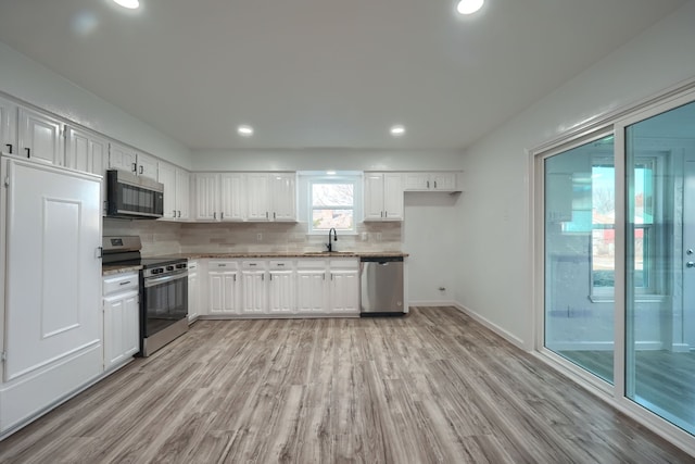 kitchen featuring white cabinets, light wood-style floors, stainless steel appliances, and decorative backsplash