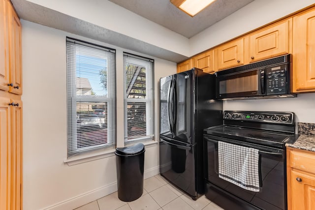 kitchen with a textured ceiling, light tile patterned floors, light brown cabinets, dark stone counters, and black appliances