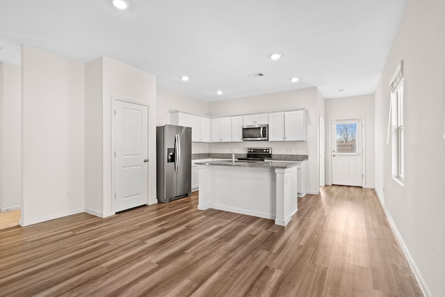 kitchen with stainless steel appliances, a center island with sink, light wood-type flooring, white cabinets, and stone counters