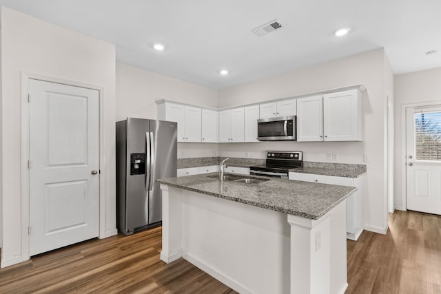 kitchen with appliances with stainless steel finishes, white cabinetry, dark hardwood / wood-style floors, and a center island with sink