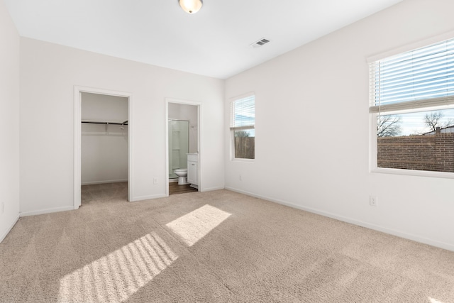 unfurnished bedroom with a walk in closet, a closet, ensuite bath, and light colored carpet