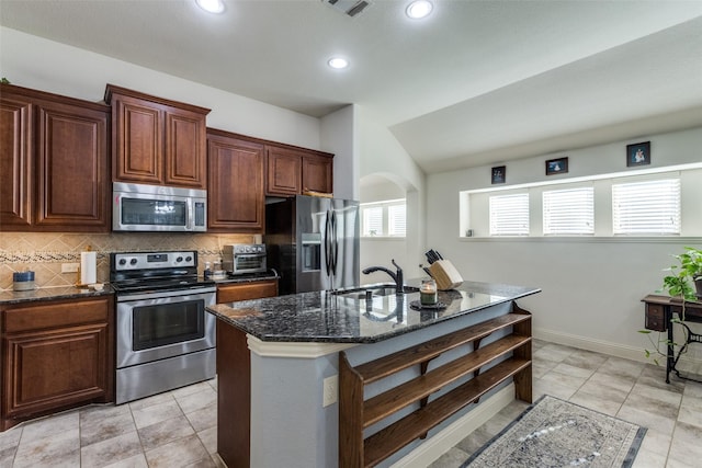 kitchen with a center island with sink, decorative backsplash, appliances with stainless steel finishes, dark stone countertops, and sink