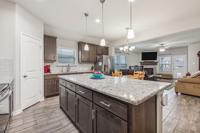 kitchen with ceiling fan with notable chandelier, a kitchen island, stainless steel appliances, tasteful backsplash, and sink