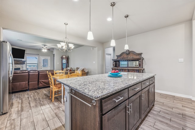 kitchen featuring a center island, stainless steel refrigerator, dark brown cabinetry, hanging light fixtures, and ceiling fan with notable chandelier