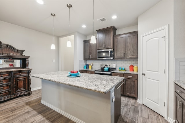 kitchen featuring a kitchen island, stainless steel appliances, tasteful backsplash, light stone counters, and dark brown cabinets