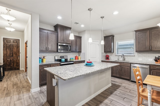 kitchen with decorative light fixtures, appliances with stainless steel finishes, sink, and a kitchen island