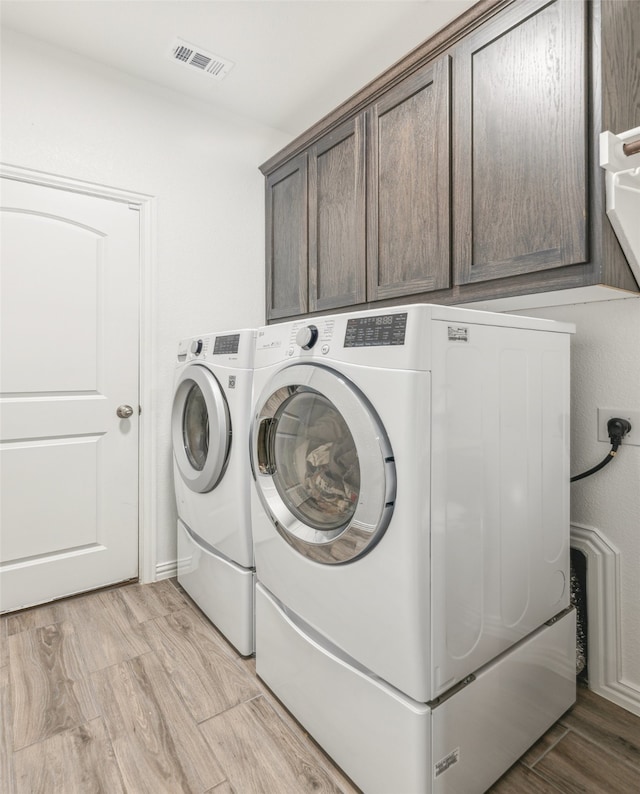 clothes washing area with light hardwood / wood-style flooring, independent washer and dryer, and cabinets