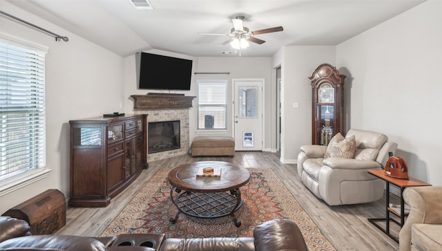 living room with ceiling fan, a stone fireplace, and light hardwood / wood-style flooring