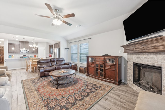 living room with lofted ceiling, a fireplace, and ceiling fan with notable chandelier