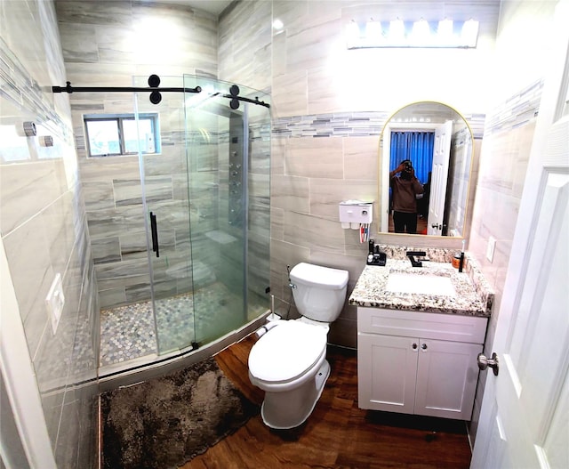 bathroom featuring toilet, wood-type flooring, walk in shower, vanity, and tile walls