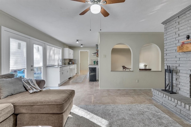 tiled living room featuring a brick fireplace, french doors, sink, ornamental molding, and ceiling fan