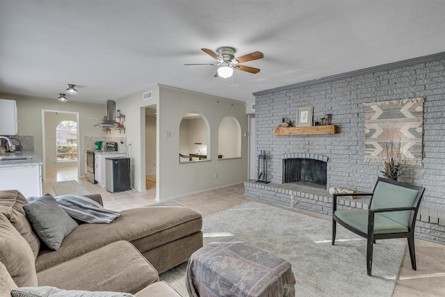 living room featuring a brick fireplace, light tile patterned floors, ceiling fan, and sink