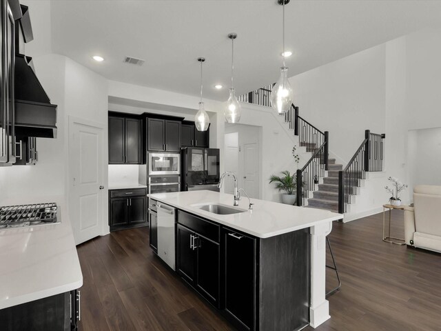 kitchen with sink, dark hardwood / wood-style floors, pendant lighting, stainless steel appliances, and a kitchen island with sink