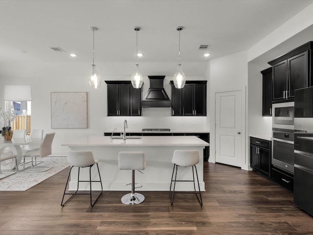 kitchen featuring a center island with sink, premium range hood, dark hardwood / wood-style flooring, sink, and oven