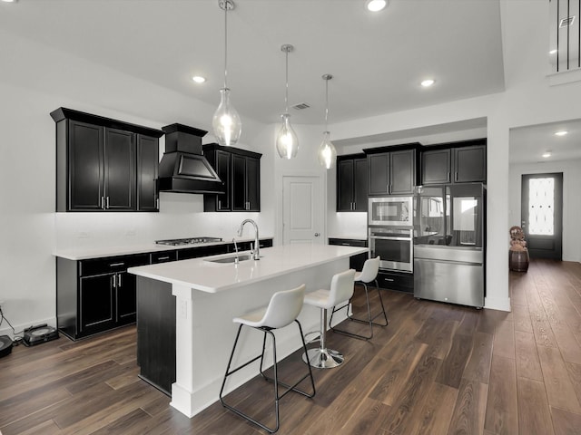 kitchen featuring sink, decorative light fixtures, an island with sink, custom exhaust hood, and appliances with stainless steel finishes