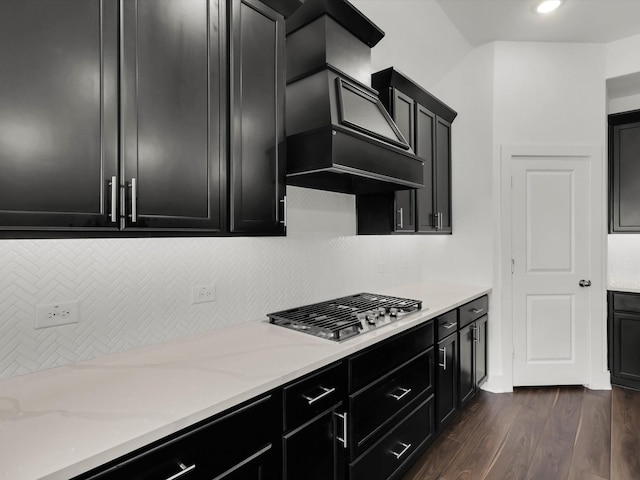 kitchen featuring light stone countertops, custom range hood, stainless steel gas stovetop, decorative backsplash, and dark hardwood / wood-style floors