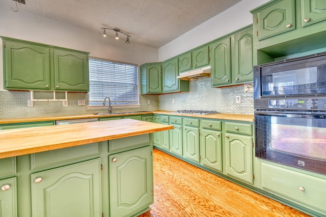 kitchen featuring under cabinet range hood, wood counters, tasteful backsplash, and a sink