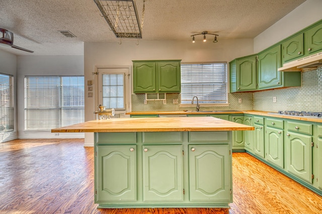 kitchen with a kitchen island, a sink, stainless steel gas stovetop, light wood-style floors, and under cabinet range hood