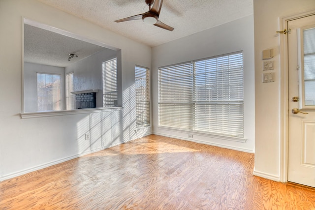 interior space featuring wood finished floors, baseboards, a fireplace, ceiling fan, and a textured ceiling