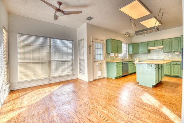 kitchen featuring visible vents, green cabinets, under cabinet range hood, light wood-style flooring, and stainless steel dishwasher