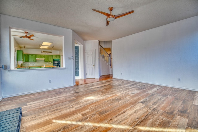 unfurnished living room featuring baseboards, stairs, light wood-type flooring, a textured ceiling, and a ceiling fan